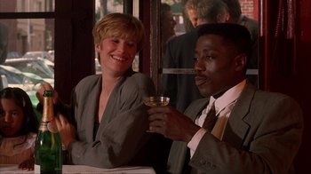 Movie still from “King of New York” (1990), directed by Abel Ferrara – A man and a woman sitting next to each other holding a glass; Medium shot, Low angle