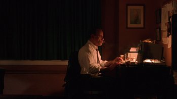Movie still from “King of New York” (1990), directed by Abel Ferrara – A man sitting at a desk in a dark room; Medium shot, Low angle