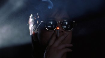 Movie still from “King of New York” (1990), directed by Abel Ferrara – A person wearing sunglasses and smoking a cigarette; Close Up shot, Low angle
