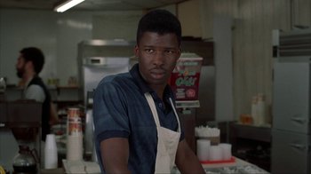 Movie still from “King of New York” (1990), directed by Abel Ferrara – A man wearing an apron standing in a kitchen; Close Up shot, Over the shoulder angle