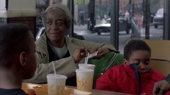 Movie still from “King of New York” (1990), directed by Abel Ferrara – An older woman sitting at a table with a young child; Medium shot, Over the shoulder angle