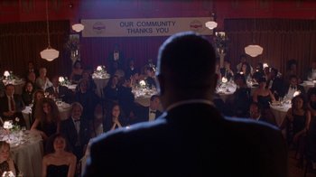 Movie still from “King of New York” (1990), directed by Abel Ferrara – A man standing in front of a crowd of people; Medium shot, Over the shoulder angle