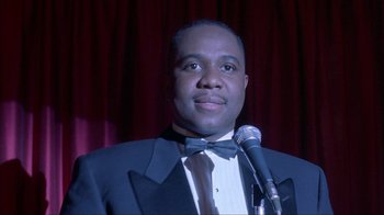 Movie still from “King of New York” (1990), directed by Abel Ferrara – A man in a suit and bow tie holding a microphone; Close Up shot, Low angle