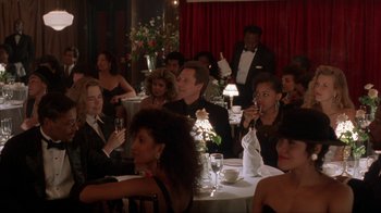 Movie still from “King of New York” (1990), directed by Abel Ferrara – A group of people sitting at a table with wine glasses; Medium shot, Over the shoulder angle