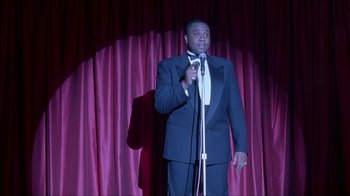Movie still from “King of New York” (1990), directed by Abel Ferrara – A man standing on a stage holding a microphone; Medium shot, Low angle