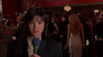 Movie still from “King of New York” (1990), directed by Abel Ferrara – A woman holding a microphone in front of a crowd; Close Up shot, Over the shoulder angle