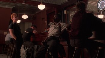Movie still from “King of New York” (1990), directed by Abel Ferrara – A group of people sitting at a bar; Wide shot, Low angle