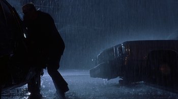 Movie still from “King of New York” (1990), directed by Abel Ferrara – A person standing next to a bus in the rain at night; Wide shot, Low angle