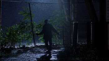 Movie still from “King of New York” (1990), directed by Abel Ferrara – A person walking in the rain near a fence; Wide shot, Low angle