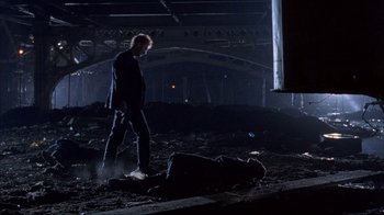 Movie still from “King of New York” (1990), directed by Abel Ferrara – A man standing next to another man laying on the ground in the dark; Wide shot, Low angle