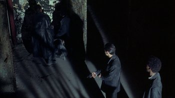 Movie still from “King of New York” (1990), directed by Abel Ferrara – A man holding a gun while standing next to a tree; Wide shot, High angle