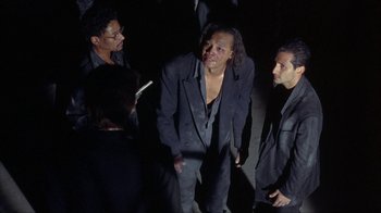 Movie still from “King of New York” (1990), directed by Abel Ferrara – A group of men standing next to each other in suits; Medium shot, Over the shoulder angle