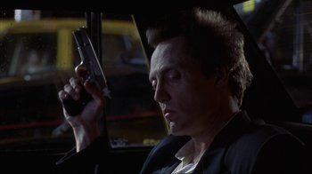 Movie still from “King of New York” (1990), directed by Abel Ferrara – A man holding a gun while sitting in a car; Close Up shot, Low angle