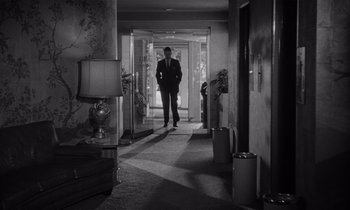 Movie still from “Kiss Me Deadly” (1955), directed by Robert Aldrich – A black and white photo of a man in a suit in a hallway; Wide shot, High angle