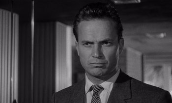 Movie still from “Kiss Me Deadly” (1955), directed by Robert Aldrich – Black and white photograph of a man wearing a suit and tie; Close Up shot, Low angle