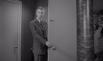 Movie still from “Kiss Me Deadly” (1955), directed by Robert Aldrich – A black and white photo of a man in a suit and tie; Medium shot, Low angle