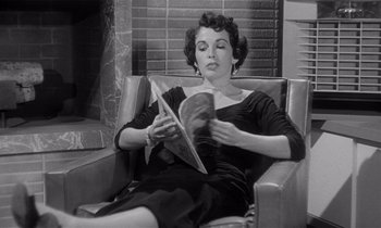 Movie still from “Kiss Me Deadly” (1955), directed by Robert Aldrich – A black and white photo of a woman reading a magazine; Medium shot, Low angle