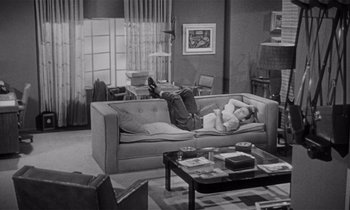 Movie still from “Kiss Me Deadly” (1955), directed by Robert Aldrich – A person laying on a couch in a living room; Wide shot, High angle