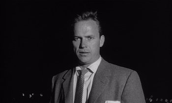 Movie still from “Kiss Me Deadly” (1955), directed by Robert Aldrich – Black and white photograph of a man in a suit and tie; Close Up shot, Low angle