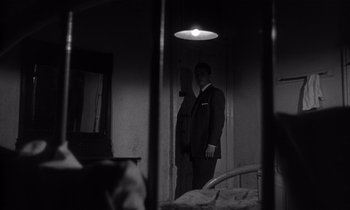Movie still from “Kiss Me Deadly” (1955), directed by Robert Aldrich – A black and white photo of a man standing in a room; Medium shot, Low angle