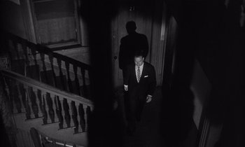 Movie still from “Kiss Me Deadly” (1955), directed by Robert Aldrich – A man in a suit and tie walking down a staircase; Wide shot, High angle