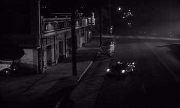 Movie still from “Kiss Me Deadly” (1955), directed by Robert Aldrich – Two cars parked on the side of the road at night; Extreme Wide shot, High angle