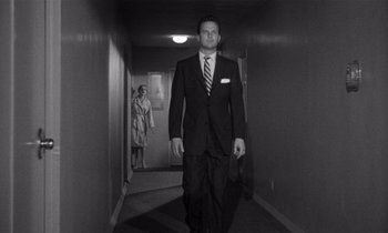 Movie still from “Kiss Me Deadly” (1955), directed by Robert Aldrich – A man in a suit and tie walking down a hall way; Wide shot, Low angle