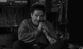 Movie still from “Kiss Me Deadly” (1955), directed by Robert Aldrich – A black and white photo of a man sitting on a couch; Close Up shot, High angle