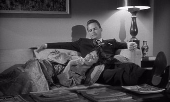 Movie still from “Kiss Me Deadly” (1955), directed by Robert Aldrich – A man and a woman laying on a couch; Medium shot, High angle