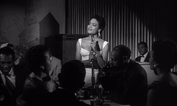 Movie still from “Kiss Me Deadly” (1955), directed by Robert Aldrich – A black - and - white photo of a woman speaking at an event; Medium shot, Over the shoulder angle