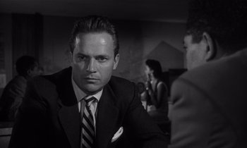 Movie still from “Kiss Me Deadly” (1955), directed by Robert Aldrich – A black and white photo of a man in a suit and tie; Close Up shot, Over the shoulder angle