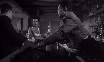 Movie still from “Kiss Me Deadly” (1955), directed by Robert Aldrich – A man and a woman sitting at a table holding hands; Medium shot, Over the shoulder angle