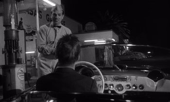 Movie still from “Kiss Me Deadly” (1955), directed by Robert Aldrich – A black and white photo of a man in a car; Medium shot, Over the shoulder angle