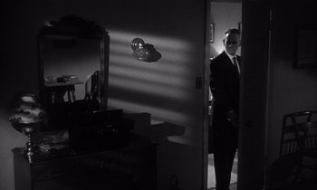 Movie still from “Kiss Me Deadly” (1955), directed by Robert Aldrich – A black and white photo of a man standing in a room; Medium shot, Low angle