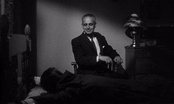 Movie still from “Kiss Me Deadly” (1955), directed by Robert Aldrich – An older man sitting in a chair next to a bed; Medium shot, Low angle