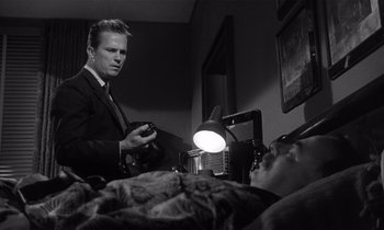 Movie still from “Kiss Me Deadly” (1955), directed by Robert Aldrich – A black and white photo of a man in a suit and tie looking at another man in a bed; Medium shot, Low angle
