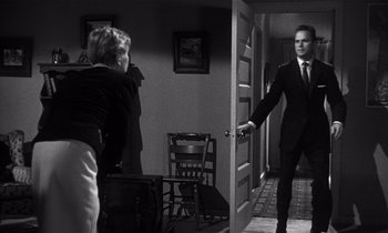 Movie still from “Kiss Me Deadly” (1955), directed by Robert Aldrich – A man in a suit and tie holding onto a door handle; Medium shot, Over the shoulder angle