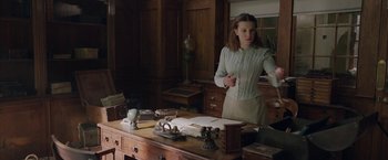Movie still from “Enola Holmes 2” (2022), directed by Harry Bradbeer – A woman standing in front of a wooden desk; Medium shot, High angle