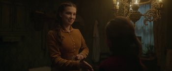 Movie still from “Enola Holmes 2” (2022), directed by Harry Bradbeer – A young woman in a brown dress is smiling at a young man; Medium shot, Over the shoulder angle