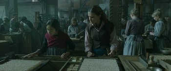 Movie still from “Enola Holmes 2” (2022), directed by Harry Bradbeer – A woman is working at a table in an old - fashioned kitchen; Medium shot, Low angle