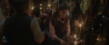 Movie still from “Enola Holmes 2” (2022), directed by Harry Bradbeer – A woman is cutting a piece of cake in front of a group of people; Medium shot, Over the shoulder angle