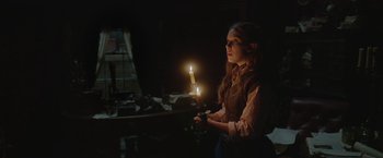 Movie still from “Enola Holmes 2” (2022), directed by Harry Bradbeer – A woman holding a lit candle in a dark room; Medium shot, Over the shoulder angle
