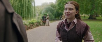 Movie still from “Enola Holmes 2” (2022), directed by Harry Bradbeer – A woman in a vest and a scarf standing on the side of a road; Close Up shot, Over the shoulder angle