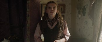 Movie still from “Enola Holmes 2” (2022), directed by Harry Bradbeer – A woman in a vest and tie standing next to a wall; Medium shot, Over the shoulder angle