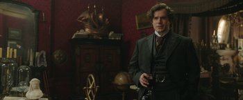 Movie still from “Enola Holmes 2” (2022), directed by Harry Bradbeer – A man standing in a room holding a wine glass; Medium shot, Over the shoulder angle