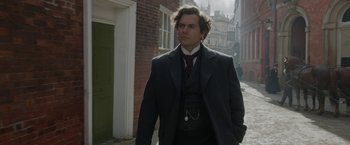 Movie still from “Enola Holmes 2” (2022), directed by Harry Bradbeer – A man wearing a suit and tie walking down a street; Medium shot, Over the shoulder angle