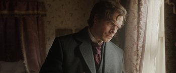 Movie still from “Enola Holmes 2” (2022), directed by Harry Bradbeer – A man in a suit and tie standing in a dimly - lit room; Close Up shot, Over the shoulder angle