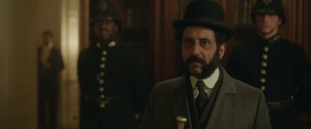 Movie still from “Enola Holmes 2” (2022), directed by Harry Bradbeer – A man in a suit and a hat standing next to another man in a uniform; Close Up shot, Over the shoulder angle