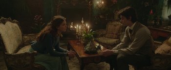 Movie still from “Enola Holmes 2” (2022), directed by Harry Bradbeer – Two people sitting at a coffee table in a living room; Medium shot, Over the shoulder angle