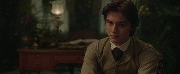 Movie still from “Enola Holmes 2” (2022), directed by Harry Bradbeer – A man in a suit and tie sitting in front of a lamp; Close Up shot, Over the shoulder angle